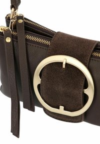 Borsa in pelle marrone con un accento di hardware circolare dorato, una tracolla in suede e due scomparti con zip per lo stoccaggio.