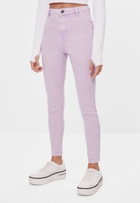 Džínsy s vysokým pasem, skořicové skinny s mírným strečem, předním zapínáním na knoflík a pěti kapsami, nošeny s bílými platformovými teniskami.