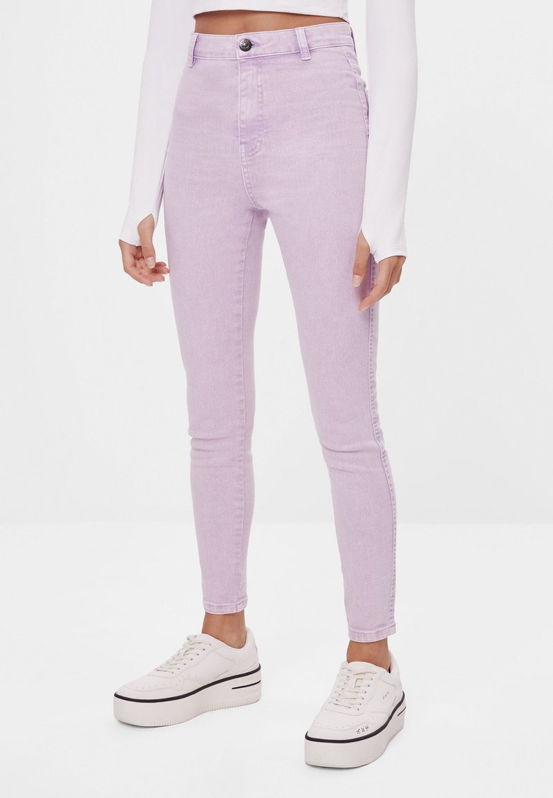 Džínsy s vysokým pasem, skořicové skinny s mírným strečem, předním zapínáním na knoflík a pěti kapsami, nošeny s bílými platformovými teniskami.