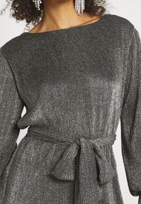 Metallisk grå klänning med ribbad textur, axelbandslös halsringning och ett knytbälte i midjan. Långa ärmar.