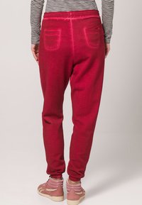 Sarkani sporta bikses ar elastīgu jostu, ribotām piedurknēm un divām aizmugures kabatām. Apvienotas ar rozā augstiem kedām. Joslains tops ir daļēji redzams.