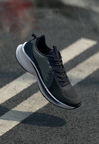 Shoe desportivo preto com parte superior em malha texturizada, atacadores e sola branca, apresentando um design leve e respirável.