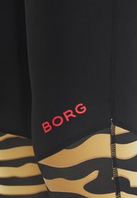 Czarno-złote kąpielówki z wzorem w paski tygrysa, czerwonym logo "BORG", gładką fakturą i kontrastującymi szwami.