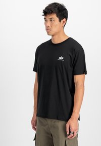 T-shirt noir à manches courtes en coton avec un col rond, arborant un petit logo blanc sur la poitrine et une étiquette sur la manche.