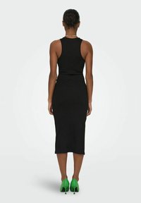 Robe midi noire à côtes avec un design sans manches, présentant une silhouette ajustée et associée à des chaussures à talons hauts vert fluo.