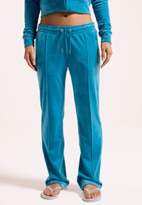 Türkise Velours-Sweatpants mit elastischem Bund, seitlichen Taschen und vertikalen Nähten für zusätzliche Textur. Ausgestellte Beinform.