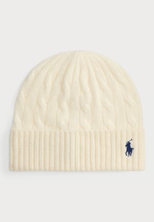 Crème kabelgebreide muts met een geribbelde boord, voorzien van een klein marineblauw logo borduursel aan de zijkant, gemaakt van een zachte wolmix.