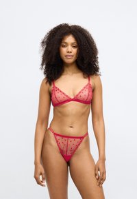 Κόκκινο διάφανο σετ εσώρουχων με τριγωνικό σουτιέν και στρινγκ, διακοσμημένο με μικρά σχέδια καρδιάς και δαντελένιες λεπτομέρειες. Ρυθμιζόμενες τιράντες.