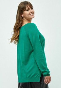 Maglione verde lavorato a maglia con una vestibilità ampia, caratterizzato da un ampio scollo e maniche lunghe, esposto su uno sfondo neutro.