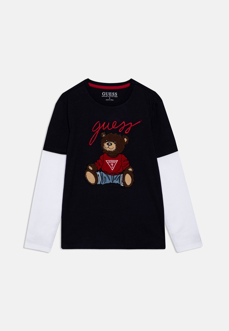 Schwarzes T-Shirt mit weißen langen Ärmel, versehen mit einem Grafik eines braunen Bären in Jeanskleidung und rotem Text "guess" in geschwungener Schrift.