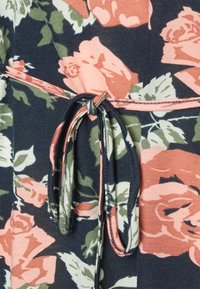Detalhe de vestido floral com um fundo azul marinho escuro e rosas em tons de pêssego e verde. Inclui um cinto de tecido atado com uma costura de destaque.
