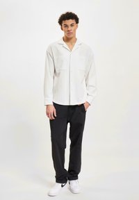 Chemise blanche à rayures avec deux poches poitrine, associée à un pantalon noir et des baskets blanches. Caractérisée par une coupe décontractée et des manches longues.