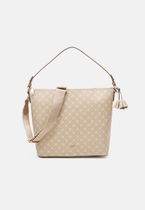 Sac à main beige à motif avec une finition texturée, doté d'une longue bandoulière réglable, de ferrures dorées et d'un pompon décoratif.