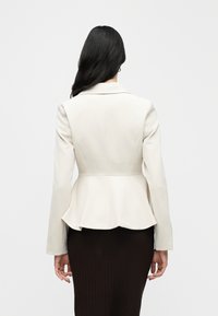 Blazer écru à basque avec un col cranté et des manches longues, en tissu lisse et un corsage ajusté, vu de dos.