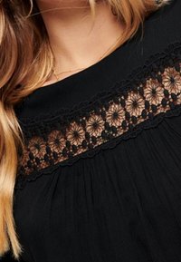 Top negro con una tela texturizada y pliegues, adornado con delicados detalles de encaje negro en el escote.