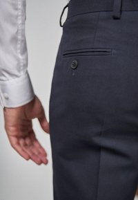 Navy-tarierte Hose mit glatter Textur, Gesäßtasche mit schwarzem Knopf und einem subtilen Biegebereich entlang der Seite.