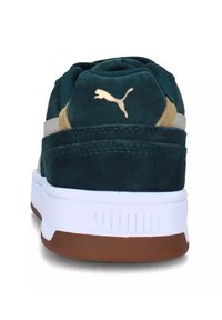 Scarpa sportiva Puma in camoscio verde scuro con accento color cuoio, suola intermedia bianca e suola esterna in gomma marrone. Presenta il logo iconico sul tallone.