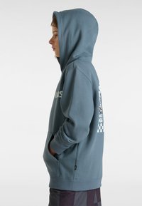 Sudadera con capucha en azul apagado, que cuenta con un bolsillo frontal, puños acanalados y un diseño gráfico con acentos a cuadros en la parte posterior.