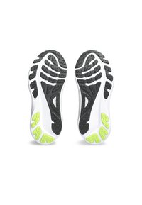 Semelles de chaussures de sport arborant un design noir et blanc, en caoutchouc texturé pour une meilleure adhérence, avec des accents verts fluo sur le dessous.