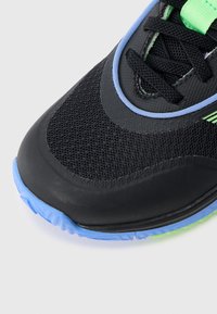 Melns sporta apavu tīkls augšdaļā ar ziliem un zaļiem akcentiem. Tai ir apaļa purngala forma un teksturēta gumijas zolīte, kas nodrošina labāku saķeri.