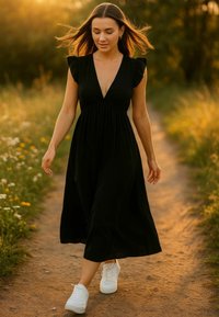 Zwarte jurk tot de knie met een diepe V-hals en ruches op de mouwen; gecombineerd met witte sneakers, terwijl ze op een onverharde weg loopt omringd door bloemen.