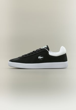 Sneaker nero basso con suola bianca e collarino sul tallone, con logo a coccodrillo e lacci su sfondo neutro.