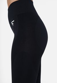 Schwarze hochtaillierte Leggings mit strukturiertem Design, die ein Logo auf der Hüfte und glatte Paneelakzente für eine konturierte Passform aufweisen.