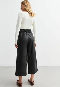 Zwarte faux leren culotte-pantalons met een elastische tailleband, gedragen met een wit langemouwen top. Dierenprint flats accentueren de look.
