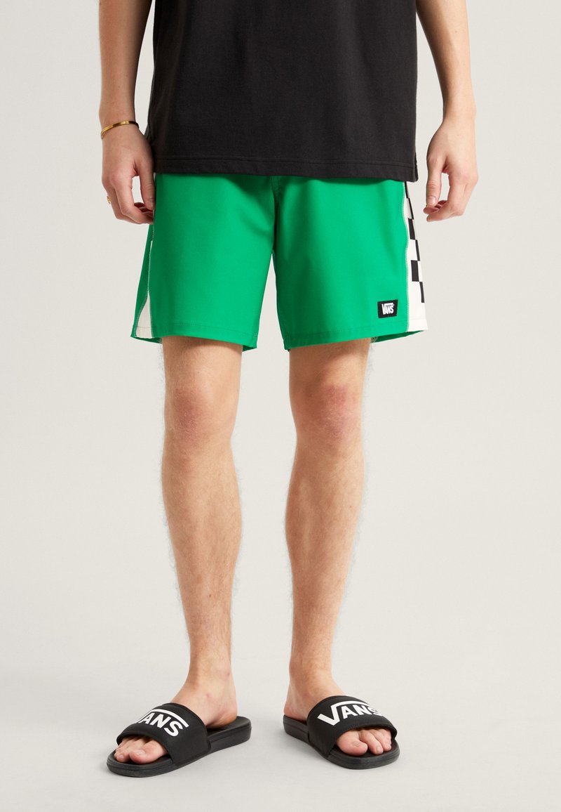 Grønne badetights med et sort og hvidt ternet mønster på siden, sammen med sorte slidesandaler med et hvidt "Vans" logo.