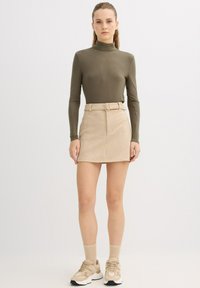 Jersey de cuello alto verde oliva de manga larga combinado con una minifalda beige con cinturón y zapatillas claras. Tejido liso con un diseño ajustado.