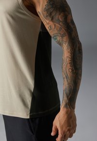 Beige og mørkegrøn tanktop med en tætsiddende pasform, der har en glat tekstur og kontrasterende farveblokke langs siden.