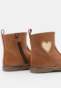 Bottines en cuir marron avec une fermeture éclair sur le côté, un patch en forme de cœur et une couture décorative sur les côtés. Semelles en caoutchouc plates.