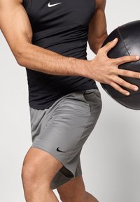 Μαύρο αθλητικό τοπ χωρίς μανίκια και γκρι σορτς, και τα δύο με λογότυπο Nike. Η στολή είναι εφαρμοστή, με λεία υφή και σχεδιασμό που επιτρέπει την αναπνοή.