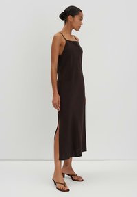 Schwarzes Slipkleid mit dünnen Trägern, geradem Ausschnitt und seitlichen Schlitzungen für Bewegungsfreiheit. Glattes Material und bodenlanges Design.