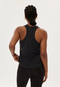 Débardeur de sport sans manches noir, en tissu lisse, encolure arrondie, design dos nageur, ourlet légèrement courbé, associé à des leggings noirs.