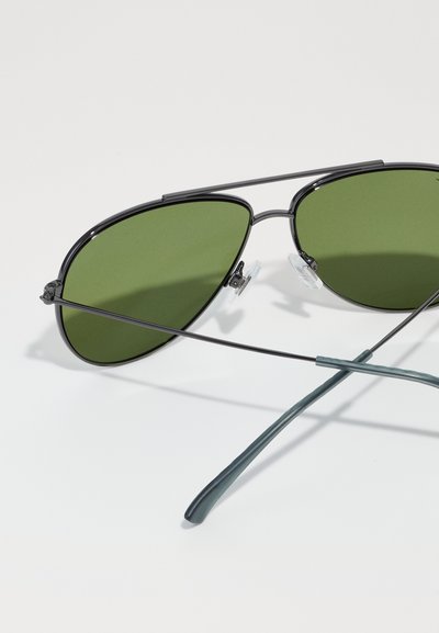 Aviator sunglasses with dark green lenses, thin black metal rims, and transparent nose pads. Temples are slender and matte teal.