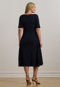 Μπλε φόρεμα έως το γόνατο, φτιαγμένο από λεία ύφασμα με ελαφριά φουσκωτή εφαρμογή και διπλωμένα μανίκια. Συνδυασμένο με ψηλοτάκουνα παπούτσια σε καφέ χρώμα.