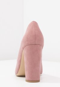 Růžová semišová lodička na vysokém podpatku s masivním podpatkem, špičatou špičkou a hladkým svrchním povrchem, úhlový pohled ze zad.