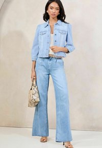 Giubbotto di jeans azzurro chiaro con taglio cropped e maniche a sbuffo, abbinato a jeans larghi azzurro chiaro. Gli accessori includono una borsa a tracolla in pelle di serpente testurizzata.