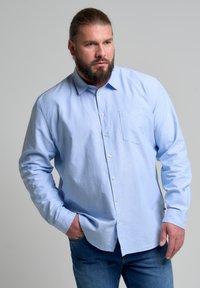 Šviesiai mėlynas medvilnės marškinėliai su įstrižiniu apykakle, ilgomis rankovėmis, krūtinės kišene ir laisvu kirpimu. Sukomplektuota su mėlynais džinsais.