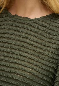 Top texturizado verde con un diseño ondulado, con rayas horizontales y un escote con puntilla. Fabricado en un material ligero y de tejido.