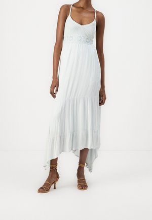 Jasnoniebieska sukienka maxi z dopasowanym dzianinowym gorsetem, koronkowymi detalami w talii oraz zwiewnym, warstwowym dołem. Połączona z beżowymi sandałami na paski.