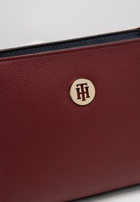 Cartera de piel burdeos con textura suave, herrajes en tono dorado y forro interior negro. Diseño compacto con costuras laterales.