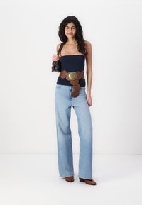 Marine offshoulder topp, brun lærbelte med sirkulær dekorasjon, lys blå vide jeans og brune hæler. Enkel håndveske holdt i hånden.