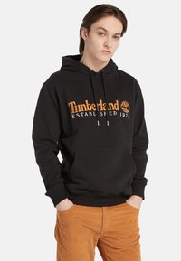 Felpa nera con cappuccio in cotone, dotata di tasca a marsupio frontale, polsini a coste e logo Timberland arancione con testo ed emblema dell'albero.