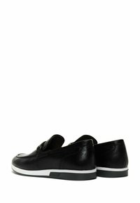 Chaussures en cuir noir à enfiler avec une finition texturée, une semelle intermédiaire blanche et un design à bout arrondi. Elles présentent un petit accent décoratif sur la partie supérieure.