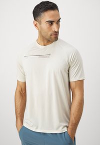 Light beige short-sleeve athletic shirt with a crew neck, featuring a subtle gray logo on the chest and a smooth, lightweight texture.