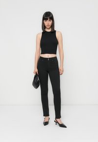 Melnā cropped tops, pieguļoši melni džinsi un melnas norādītā zābaki. Tur rokās mazu melnu somu. Gluda auduma ar elegantu siluetu.