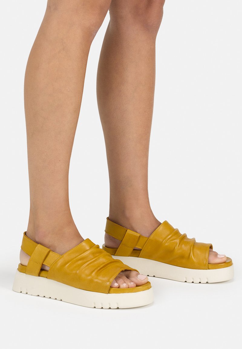 Gelbe Leder-Sandalen mit strukturiertem Design, offener Zehenpartie und verstellbaren Riemen, ausgestattet mit einer dicken weißen Sohle mit Rillen.