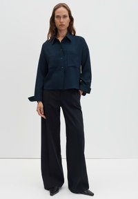 Navy blue button-up shirt with a textured pattern, featuring two front pockets and a collared neckline, paired with wide-legged black trousers.